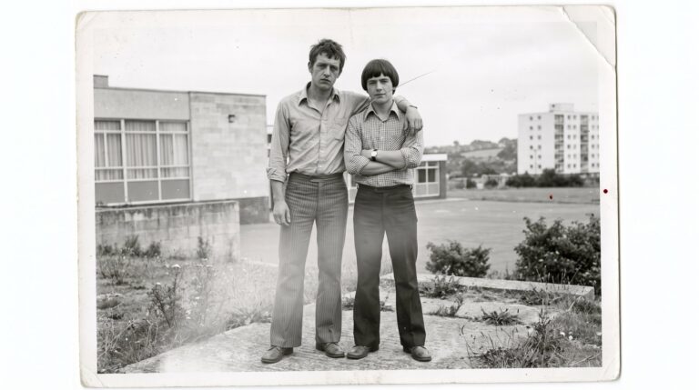 Doi tineri cu pantaloni evazați, în fața unei școli (imagine generată cu AI)